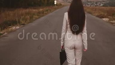 一位身材苗条的女商人，手里拿着黑色公文包，穿着裤子，穿着白色的高跟鞋，背在沥青上
