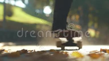 独自玩滑板的人在户外的落叶上骑滑板。 关注前景。 慢动作。