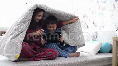 母亲和儿子一起在毯子下面的平板电脑上看电影