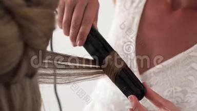 发型师在美容工作室里给年轻女人做发型时，用发铁做卷发。 快关门。 美容师制作