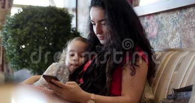 幸福的家庭，妈妈和女儿一起休息，幸福的妈妈和女儿用智能手机，坐在沙发上拥抱，