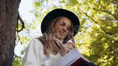 英俊的年轻女子戴着时尚的太阳镜，坐在绿色公园里，在她的<strong>奶制品</strong>里写着一些想法。