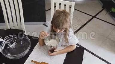 上图是一个小孩在做面团时用勺子搅拌面粉，妈妈`助手。 美丽的女孩混在一起