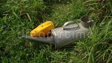 夏日的乡村风景，有一片盛开的草地。 一个黄色的小塑料浇水罐和一个大金属浇水罐躺在格栅上