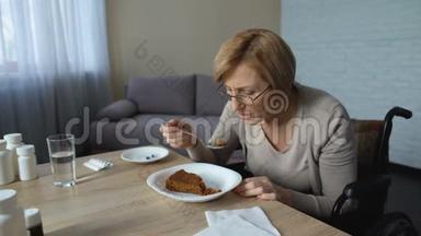 孤独的老奶奶坐在轮椅上慢慢地在桌旁吃着午饭