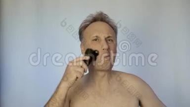 一个人用电动剃须刀刮胡子。 早上在镜子前。 他照顾他的外表。