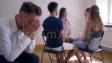 小组治疗，悲伤的男人用双手捂住脸，周围坐在椅子上的人的背景