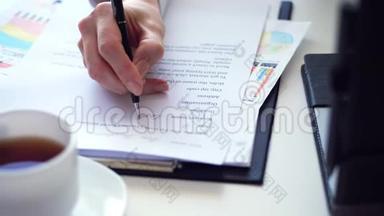 在办公桌上用笔记本电脑时，`的手在写东西。 在白色桌面上有一个白色的