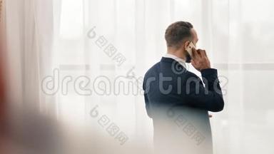 男商人用智能手机触摸屏接听来电，站在前窗