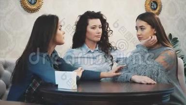 三个可爱的漂亮女孩坐在咖啡馆里。 在这期间，他们聊天，直接在眼睛里看到。 漂亮的黑色长发