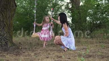 美丽的小女孩和她的母亲骑在秋千上，在公园里，在大自然中