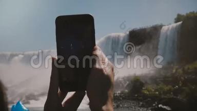 慢动作特写镜头，人类双手捧着黑色智能手机，拍摄史诗般的尼亚加拉大瀑布风景..