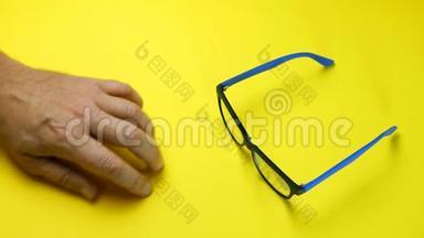 人类双手搜索，在蓝色塑料框架中找到并拿走眼镜。 在黄色背景上。