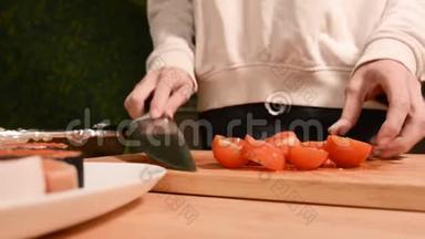 女孩的特写`她的手在家里的厨房里用木切板刀小樱桃番茄用刀。 家庭