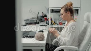 办公室里的成熟女人在编织。 一个女人在办公室打毛衣，休息时坐在办公室里