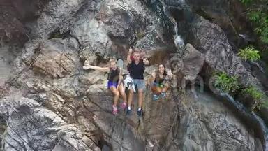 年轻的游客在瀑布旁休息，手在镜头中挥舞。 高清空中慢速运动。 泰国。
