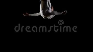 穿着白色衣服、黑色背景的英俊男体操运动员，在蹦床上缓慢地跳跃，表演翻转和跳跃