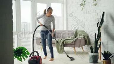 有魅力的年轻女士在家中打扫房间时，正在通过耳机跳舞和唱歌，女孩是。