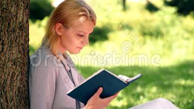 那个女孩从坐在公园草地上的笔记本上看书。 女学生准备在公园上课。 这就是