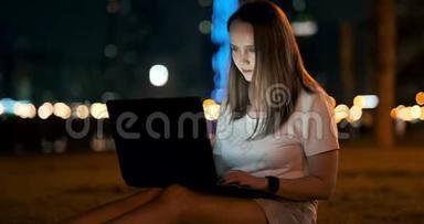 女开发商晚上坐在公园里看着笔记本电脑屏幕写代码