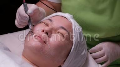 不信任。 一位亚洲貌美的女人在脸上做了<strong>电流</strong>清洗。 一个美容师用电<strong>器</strong>应用程序的工作