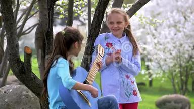 少年女孩弹牛仔裤吉他，在春天的公园里唱歌