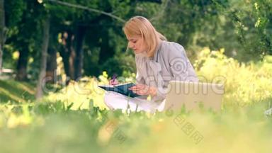 一个女人坐在公园的草地上写着笔记本。 一个学生坐在公园里准备考试