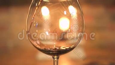 在带有蜡烛背景的晚餐中，在空酒杯中倒入红酒。 红酒从瓶子里倒出来