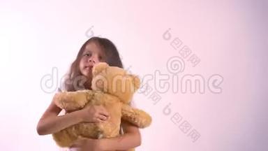 年轻开朗的小女孩和毛绒玩具熊玩耍，把他抱起来，微笑着，被隔离在亮粉色的工作室里