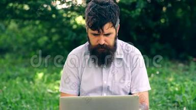 那个留胡子的人在公园里<strong>用笔</strong>记本电脑工作。 一个学生在草地上坐着，情绪激动地<strong>用笔</strong>记本电脑工作