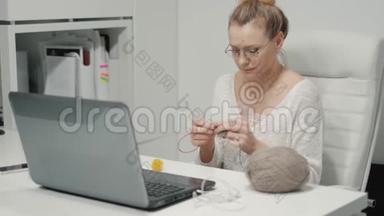 办公室里的成熟女人在编织。 一个女人在办公室打毛衣，休息时坐在办公室里