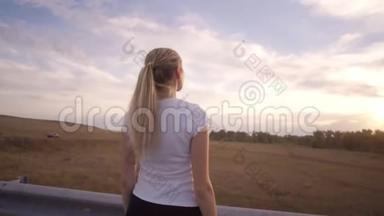 一个穿着白色t恤和长发的运动女孩在城外一条几乎空荡荡的<strong>跑道上</strong>做呼吸运动