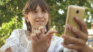 年轻女孩在平板电脑上和朋友聊天。 美丽的女孩在智能手机上写一封信，在春天，夏天，公园里。