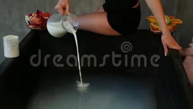 健身女孩把牛奶从玻璃杯倒入黑色浴缸，热水