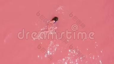 空中观景。 一个美丽的年轻女孩躺在粉红色的湖里，一件比基尼，太阳镜，粉红色的清澈的水，一张最高的风景。