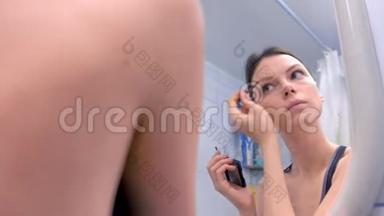 美丽的黑发女人在镜子前的浴室里画眉毛。