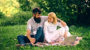 女孩和她的男朋友坐在公园的毯子上聊天。 一个男孩抱着一个女孩坐在毯子上