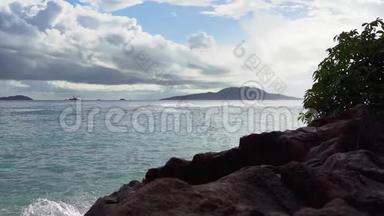 塞舌尔。 普拉斯林岛。 泡沫波浪在沙滩上翻滚。 前景中的石头。 慢动作。