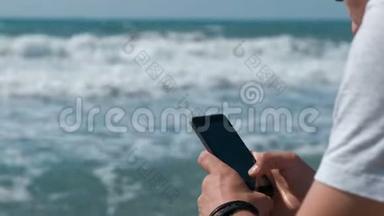 年轻人在坐在海边的大石头上的<strong>手机</strong>上<strong>输入</strong>一条信息。