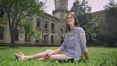 美丽的年轻女大学生，留着长发，坐在大学附近公园的草地上，微笑着，快乐着，