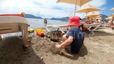 可爱的微笑的2岁男孩在海边玩沙子的4K镜头