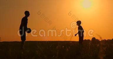 日落时分，父亲和儿子在公园里踢足球，在明亮的阳光下剪影，动作缓慢