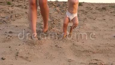 穿着尿布的小婴儿第一步走在沙滩上，手牵着妈妈。 腿。 特写