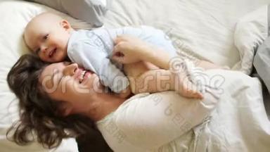 女人挠痒痒，拥抱她那岁的儿子。 阳光家庭早晨<strong>妈妈</strong>和宝宝在床上。 <strong>母亲节</strong>