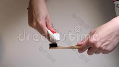 带有新鲜白色牙膏的牙刷黑色刚毛。 把牙膏从管子里挤到木制牙刷上。