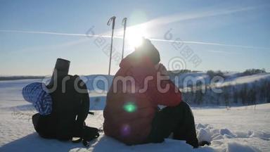 人类旅行者坐在冬天的山上的悬崖上，<strong>喝热水</strong>瓶里的茶。 年轻人的后景
