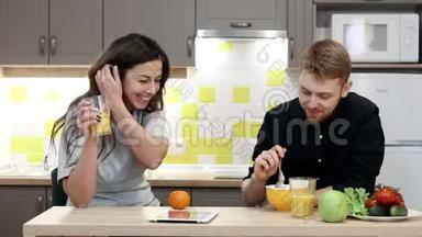 年轻夫妇带着平板电脑坐在厨房的<strong>桌子</strong>旁吃<strong>早餐</strong>。