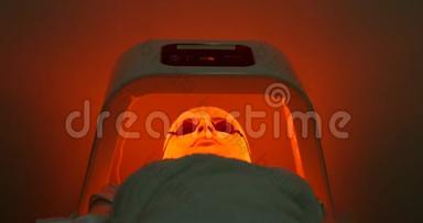 在水疗沙龙接受LE D光疗的带面膜和眼镜的女人的正面视图。 美容治疗和美容