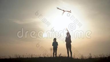 幸福的家庭母女在日落时分在草地上放风筝。 有趣的家庭时光。 友好家庭的概念