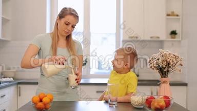 美丽的白种人妈妈，留着长长的白发，为她穿着黄色衬衫的可爱儿子<strong>倒了</strong>一杯牛奶。 现代